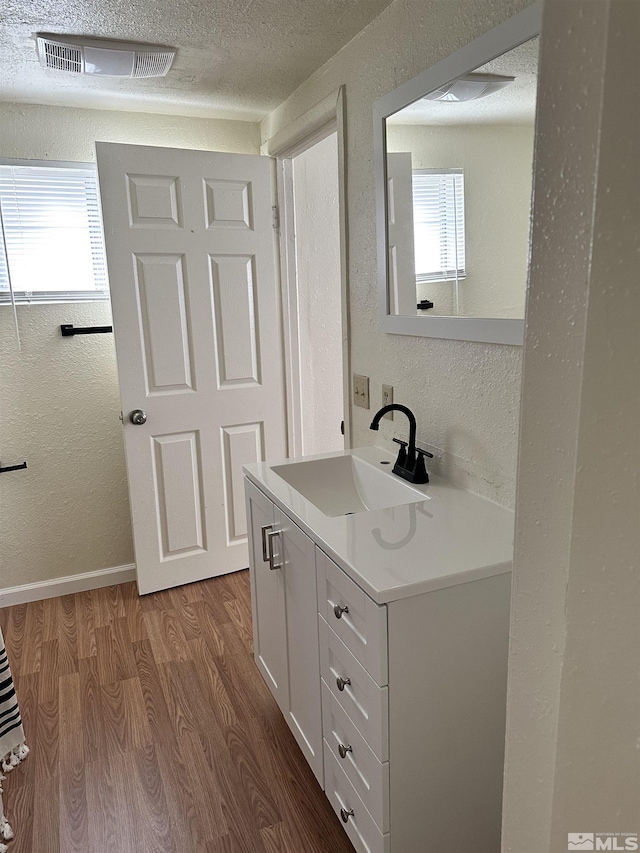 bathroom with visible vents, a textured ceiling, a textured wall, and wood finished floors