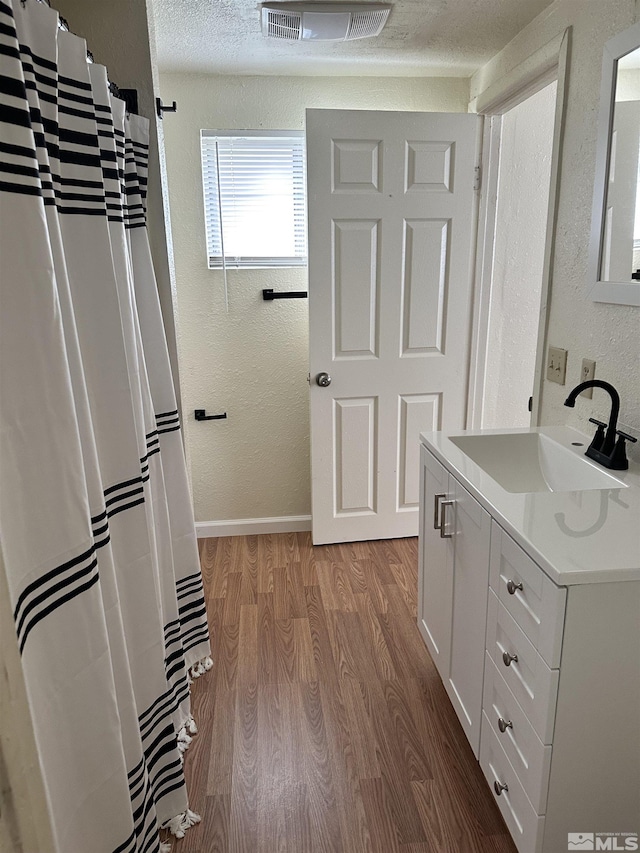 bathroom with vanity, wood finished floors, visible vents, baseboards, and a textured wall