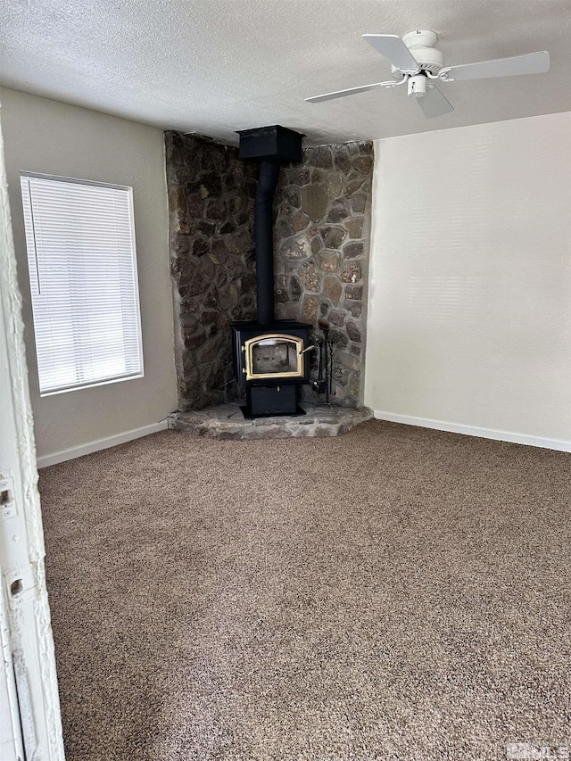 unfurnished living room with a wood stove, carpet, baseboards, and a textured ceiling