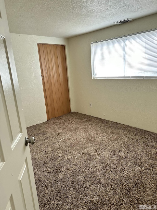 spare room featuring carpet flooring, a textured wall, visible vents, and a textured ceiling