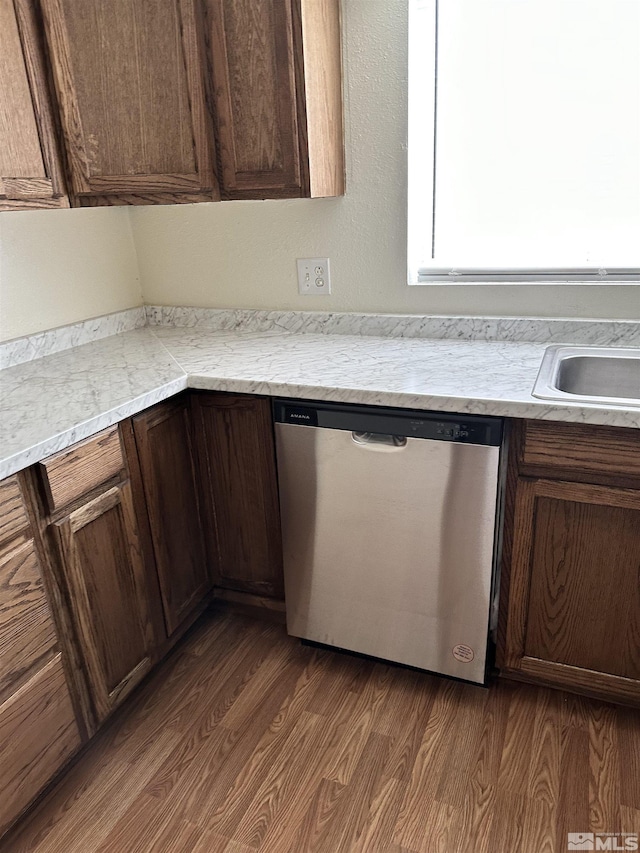 kitchen with stainless steel dishwasher, dark wood-type flooring, light countertops, and a sink