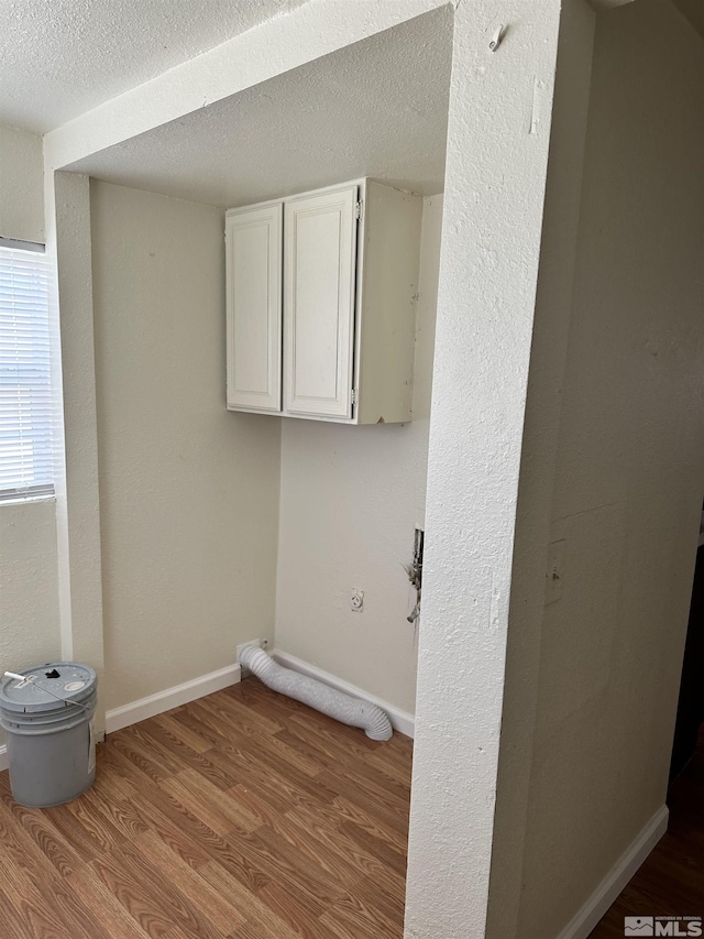 washroom with cabinet space, a textured ceiling, baseboards, and wood finished floors