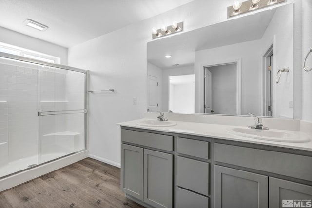 bathroom featuring double vanity, a sink, a stall shower, and wood finished floors