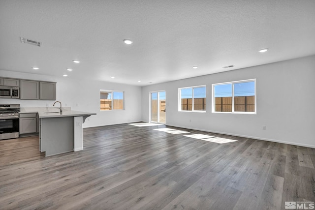 kitchen featuring open floor plan, stainless steel appliances, gray cabinetry, a sink, and visible vents