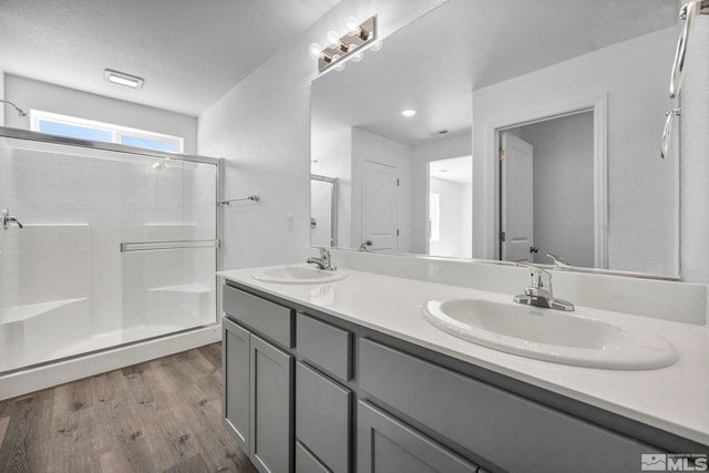 full bathroom featuring a shower stall, double vanity, wood finished floors, and a sink