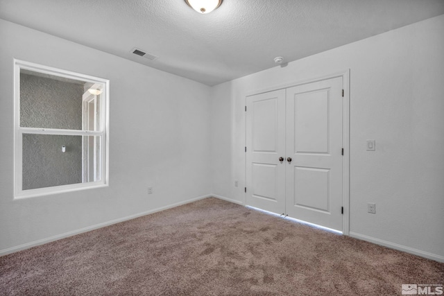 unfurnished bedroom with baseboards, a textured ceiling, carpet floors, visible vents, and a closet