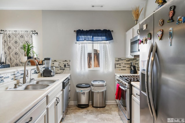 kitchen with a sink, backsplash, appliances with stainless steel finishes, white cabinets, and light countertops