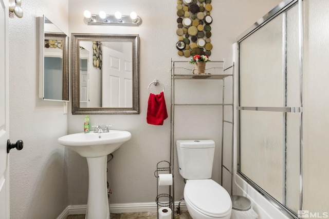 bathroom with toilet, baseboards, a shower with shower door, and a sink