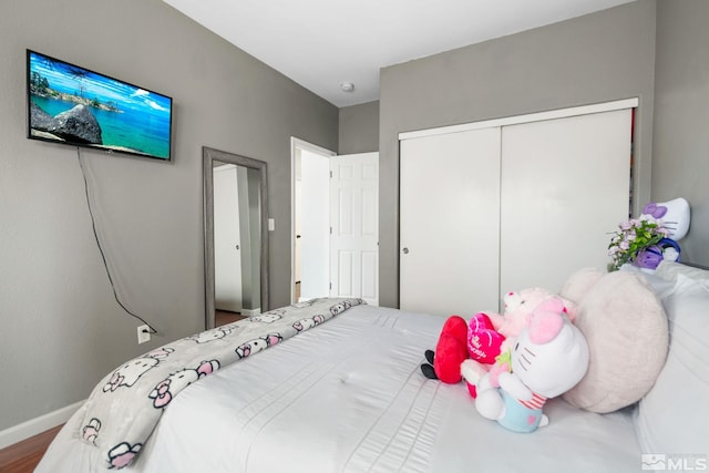 bedroom with wood finished floors, baseboards, and a closet