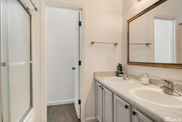 full bath with double vanity, wood finished floors, baseboards, and a sink