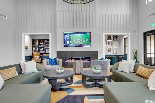 living room with a glass covered fireplace, visible vents, and a towering ceiling