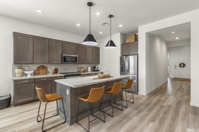 kitchen with light wood finished floors, dark brown cabinets, tasteful backsplash, and appliances with stainless steel finishes
