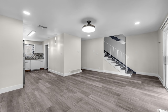 unfurnished living room with stairs, wood finished floors, visible vents, and baseboards