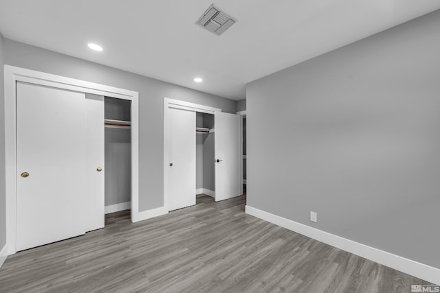 unfurnished bedroom with wood finished floors, baseboards, visible vents, recessed lighting, and multiple closets