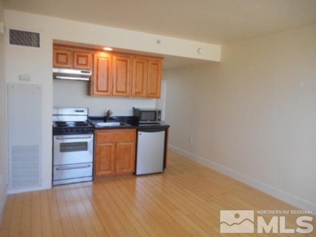 kitchen featuring under cabinet range hood, visible vents, a sink, light wood-style floors, and appliances with stainless steel finishes