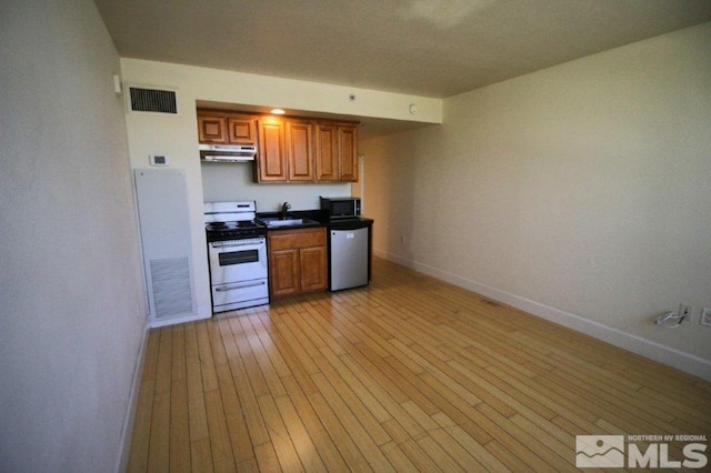 kitchen featuring under cabinet range hood, dishwashing machine, a sink, gas range oven, and baseboards
