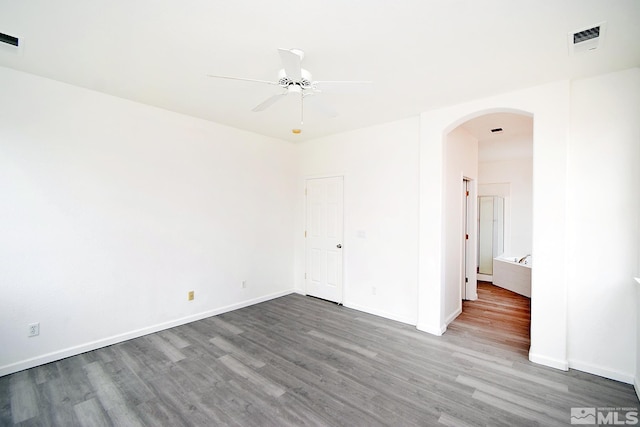 empty room with baseboards, arched walkways, ceiling fan, visible vents, and wood finished floors