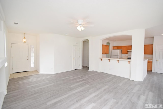 unfurnished living room featuring baseboards, arched walkways, light wood finished floors, visible vents, and ceiling fan