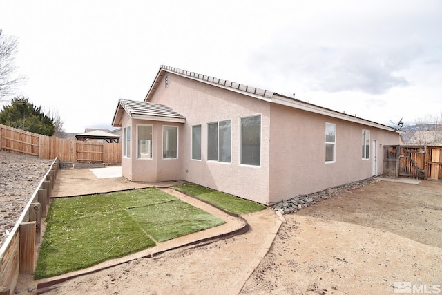 back of house featuring a fenced backyard, a lawn, stucco siding, and a patio area