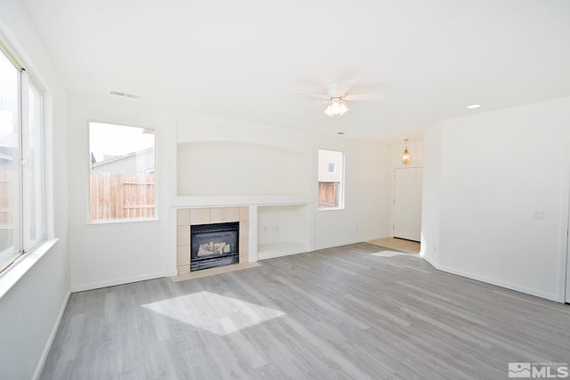 unfurnished living room with a fireplace, light wood finished floors, ceiling fan, and visible vents
