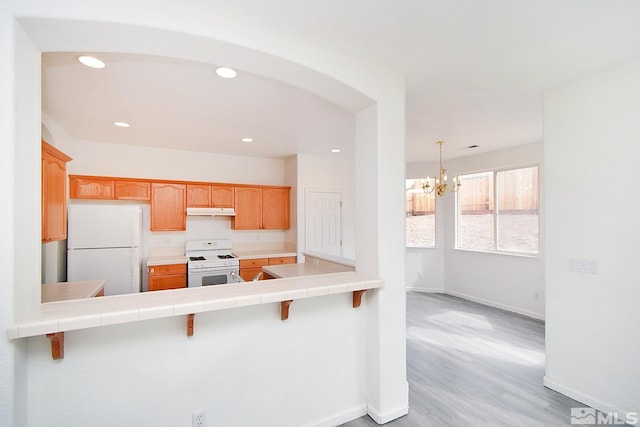 kitchen featuring white appliances, baseboards, under cabinet range hood, tile countertops, and an inviting chandelier