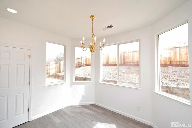 unfurnished dining area featuring wood finished floors, baseboards, a chandelier, and visible vents