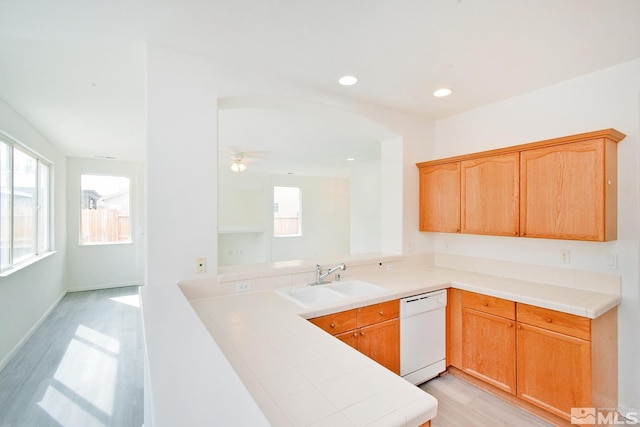 kitchen featuring light wood-style flooring, a peninsula, dishwasher, tile countertops, and a sink