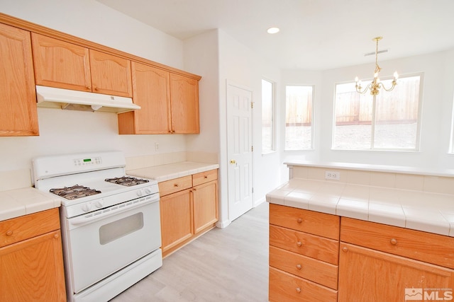 kitchen with visible vents, under cabinet range hood, gas range gas stove, light wood-style floors, and an inviting chandelier
