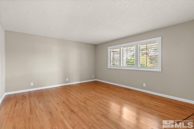 empty room with baseboards, light wood-type flooring, and a textured ceiling