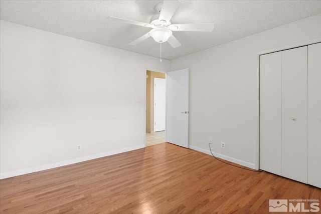 unfurnished bedroom with a ceiling fan, wood finished floors, baseboards, a closet, and a textured ceiling