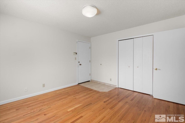 unfurnished bedroom with a closet, baseboards, a textured ceiling, and wood finished floors
