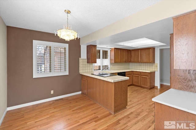 kitchen with light wood finished floors, decorative backsplash, brown cabinets, a peninsula, and an inviting chandelier