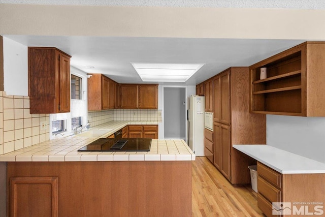 kitchen with decorative backsplash, a sink, freestanding refrigerator, a peninsula, and black electric cooktop