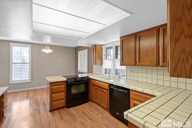 kitchen featuring brown cabinets, a peninsula, black appliances, and light wood-style floors