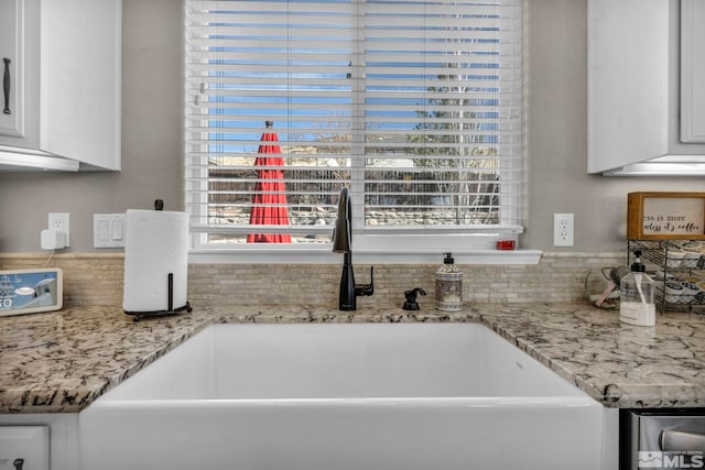 kitchen featuring white cabinetry, a sink, and light stone counters