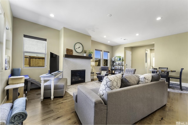 living area featuring a glass covered fireplace, recessed lighting, wood finished floors, and baseboards