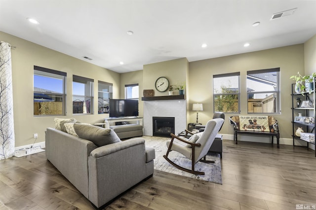 living room with a glass covered fireplace, visible vents, plenty of natural light, and dark wood finished floors