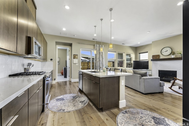 kitchen with an island with sink, a sink, stainless steel appliances, light countertops, and backsplash