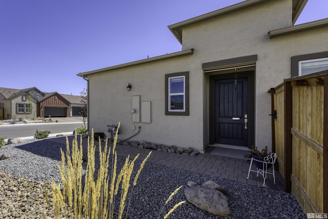 view of exterior entry with stucco siding and fence