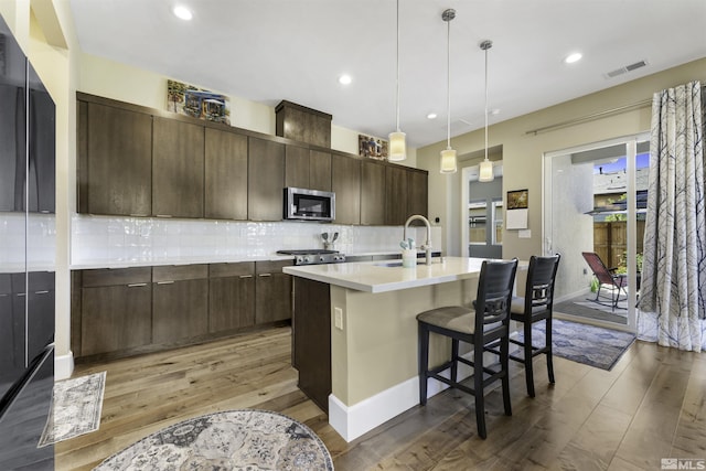 kitchen featuring visible vents, a sink, stainless steel microwave, backsplash, and light countertops
