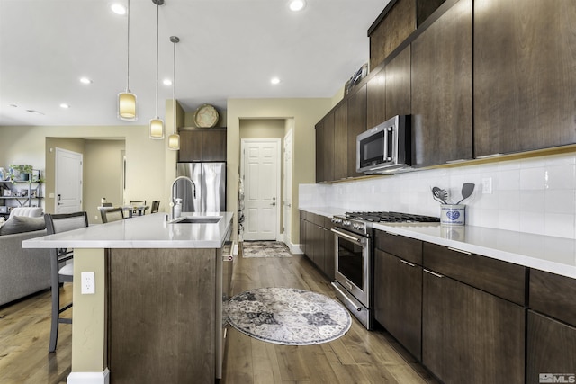 kitchen featuring stainless steel appliances, dark brown cabinetry, open floor plan, a kitchen bar, and tasteful backsplash