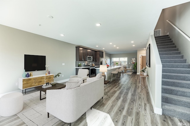 living room featuring visible vents, baseboards, stairs, recessed lighting, and light wood-type flooring