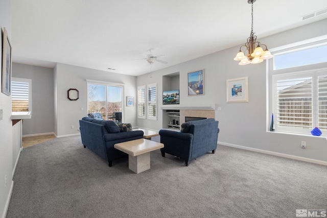 living room featuring ceiling fan with notable chandelier, baseboards, visible vents, light carpet, and a fireplace