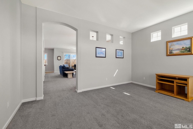 unfurnished room with arched walkways, baseboards, dark carpet, and plenty of natural light