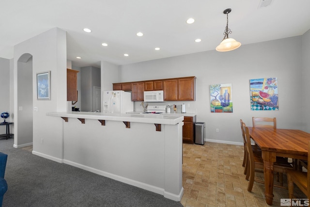 kitchen with light countertops, a breakfast bar area, white appliances, baseboards, and a peninsula