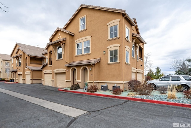 view of front of home with stucco siding, driveway, a garage, and cooling unit