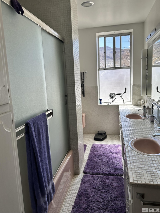full bath with tile walls, a shower stall, tile patterned floors, a sink, and wainscoting