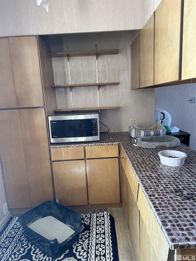 kitchen with a textured wall, stainless steel microwave, dark countertops, and open shelves