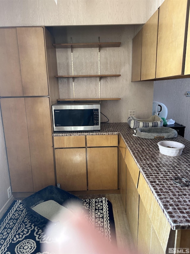 kitchen featuring stainless steel microwave, a textured wall, and open shelves