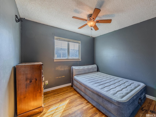 bedroom featuring baseboards, a ceiling fan, wood finished floors, and a textured ceiling